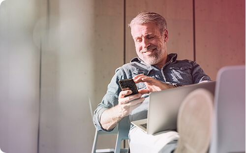 Lächelnder Mann sitzt bequem mit seinem Handy in der Hand