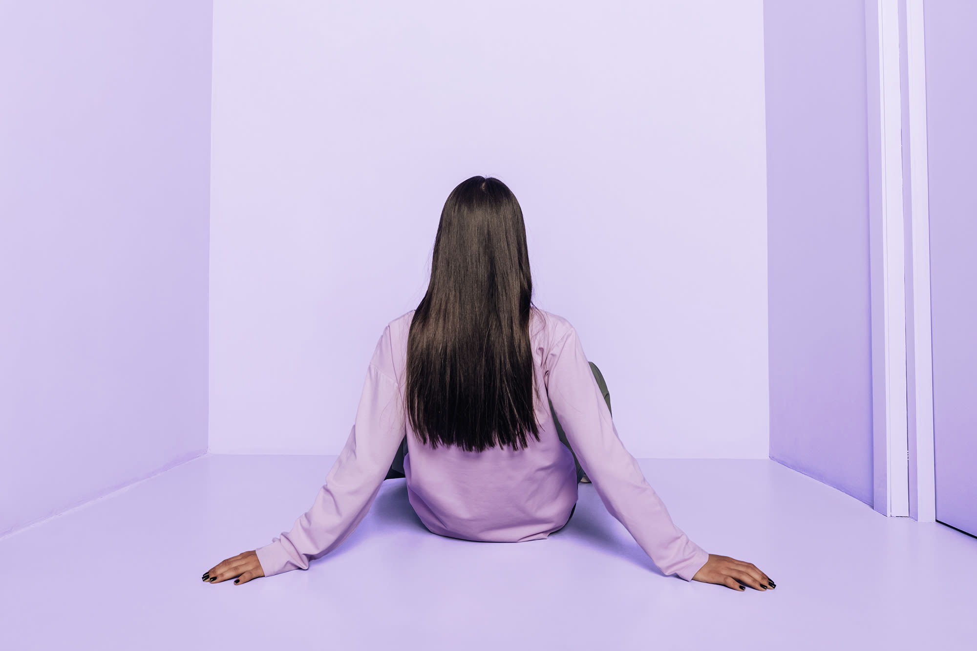 Ženska sedi v vijolični sobi s hrbtom proti kameri.