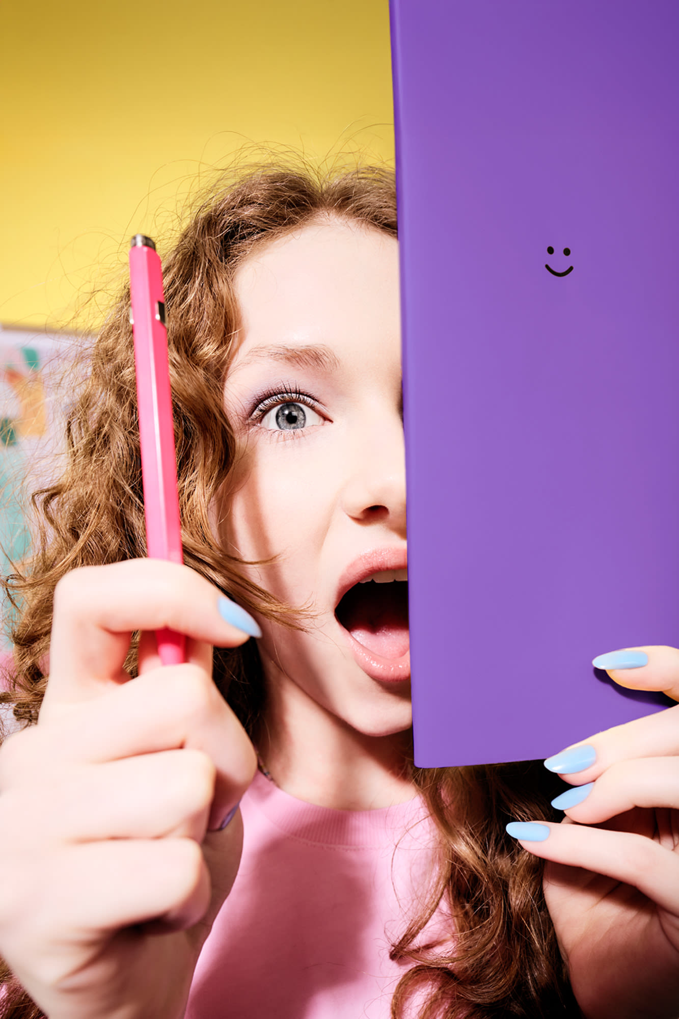 Mlada ženska z rdečimi kodri, ki v rokah drži vijolično knjigo z nasmeškom.