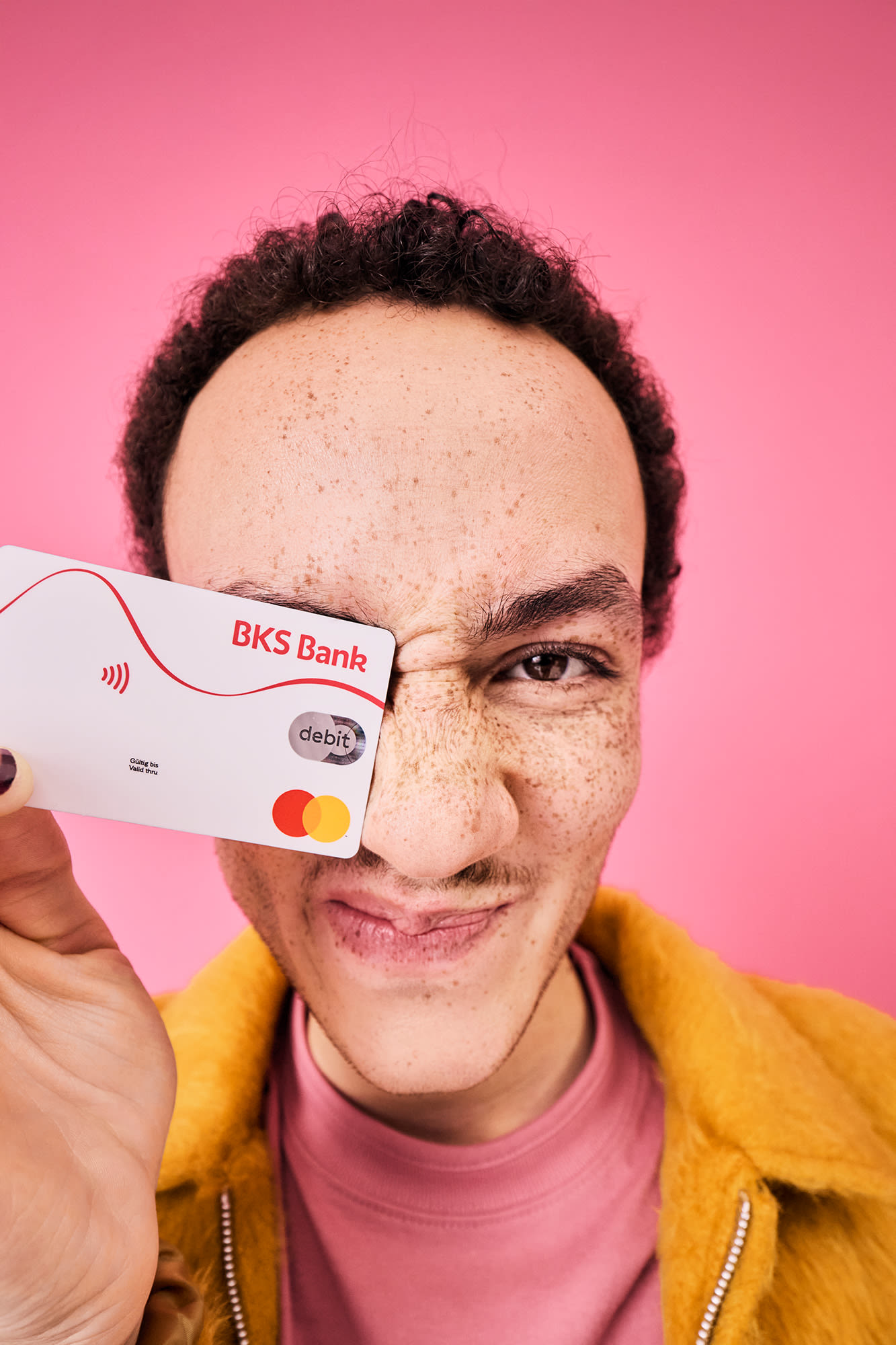 Moški z debetno kartico BKS pred rožnatim ozadjem - brezstično plačevanje z banko BKS.
