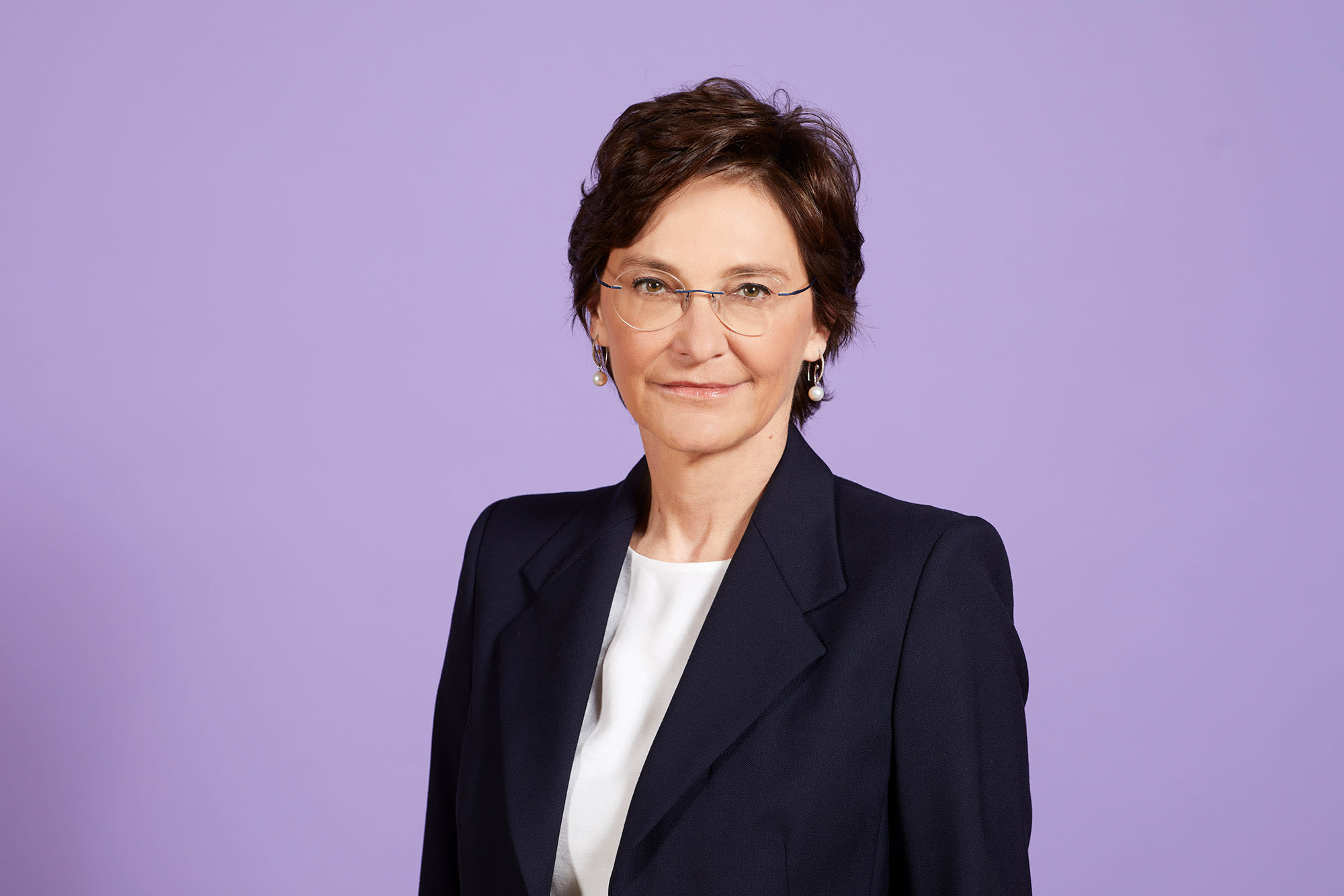 Claudia Höller in schwarzem Blazer vor lila Hintergrund.