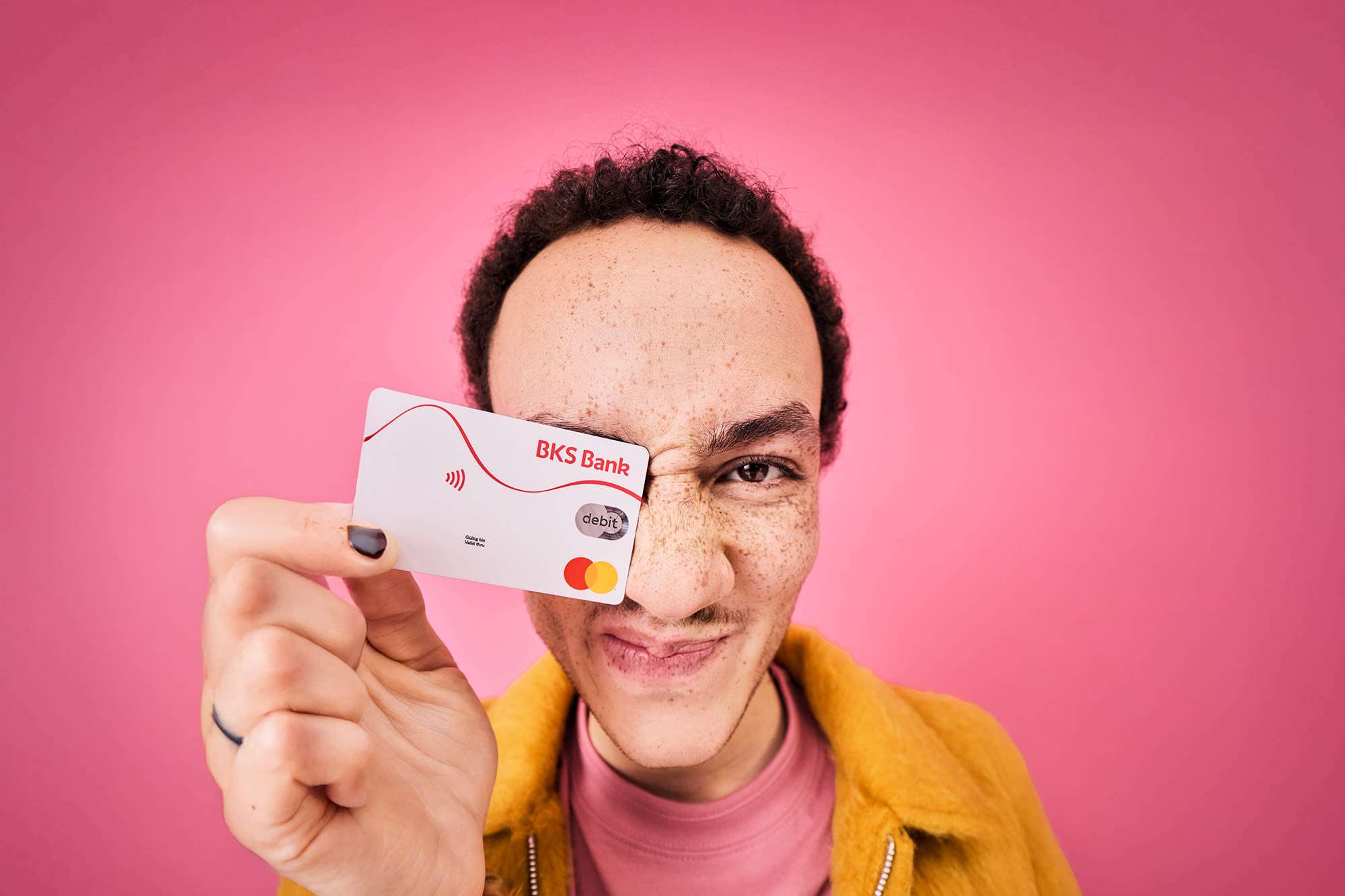 Moški z debetno kartico BKS pred rožnatim ozadjem - brezstično plačevanje z banko BKS.