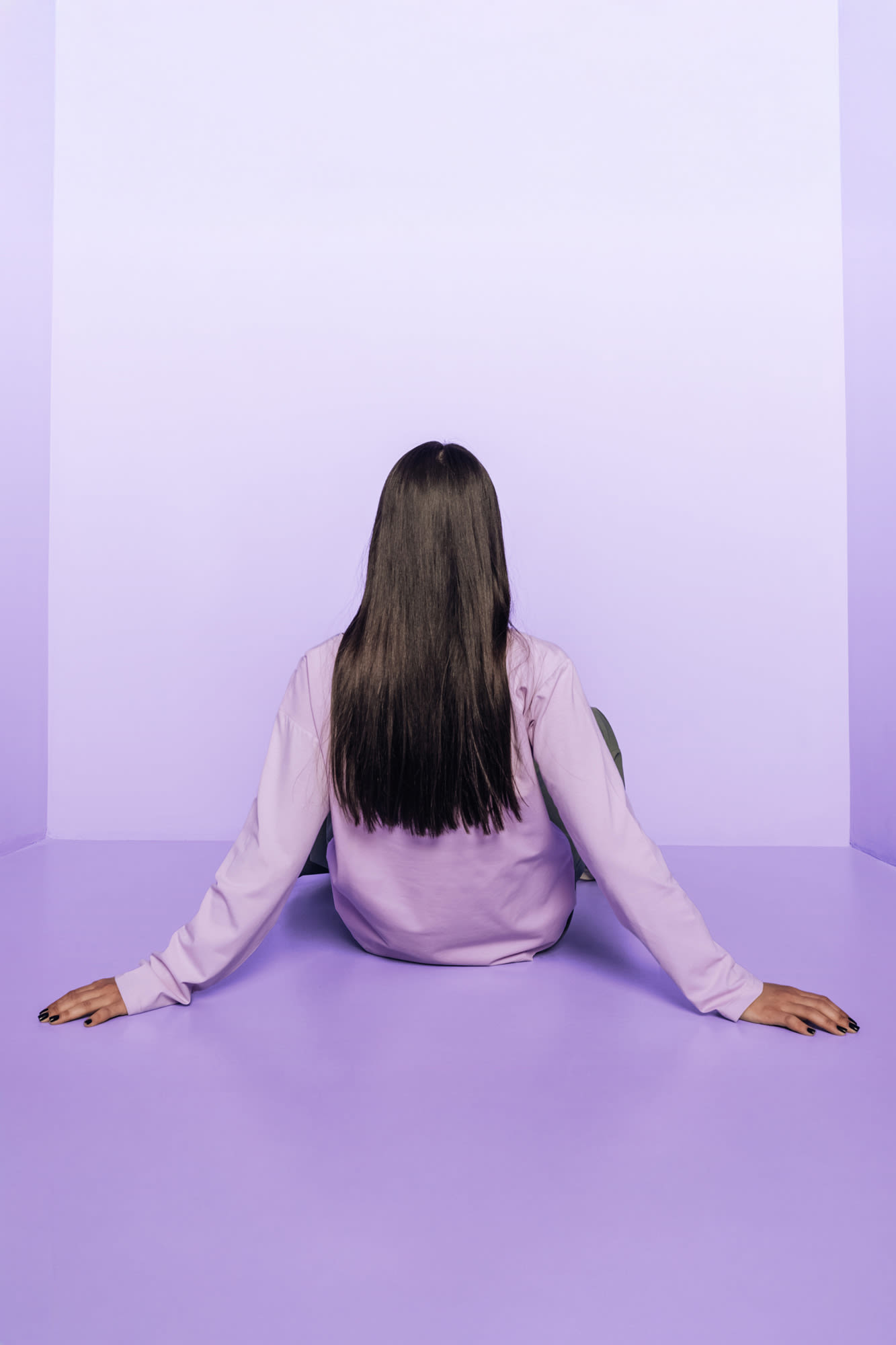 Ženska sedi v vijolični sobi s hrbtom proti kameri.