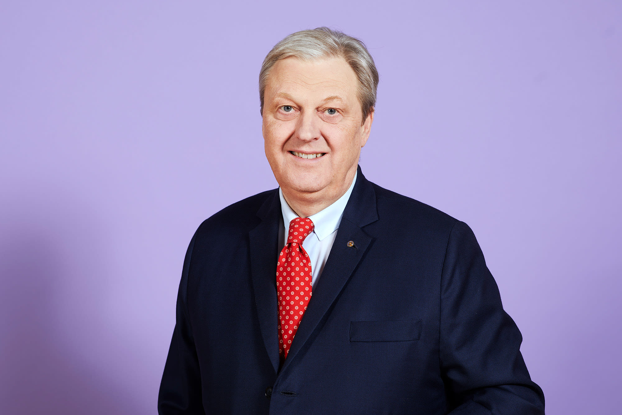 Nikolaus Juhasz im Anzug vor lila Hintergrund.