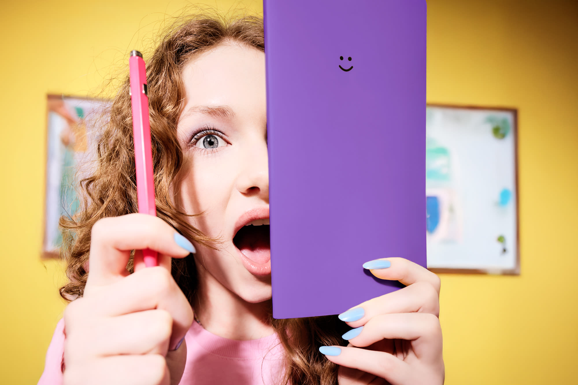 Mlada ženska z rdečimi kodri, ki v rokah drži vijolično knjigo z nasmeškom.